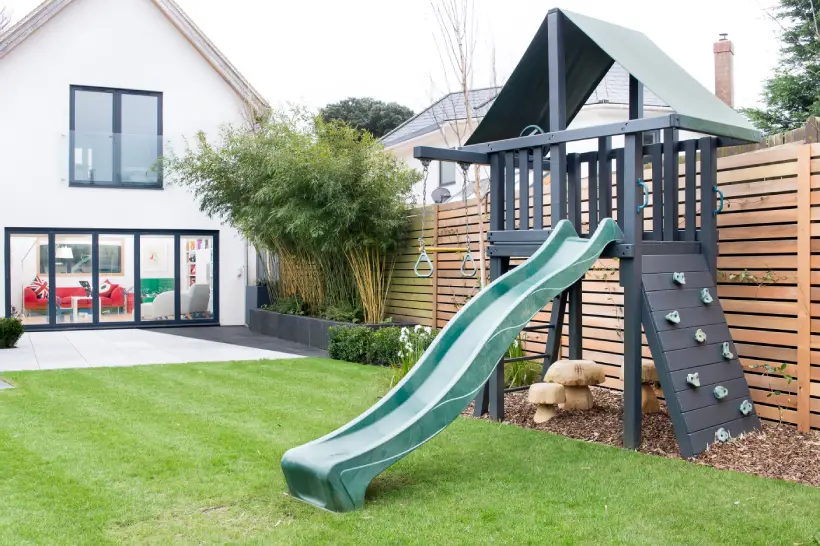 a child's slide and climbing frame in a garden with mushroom stool ></p>